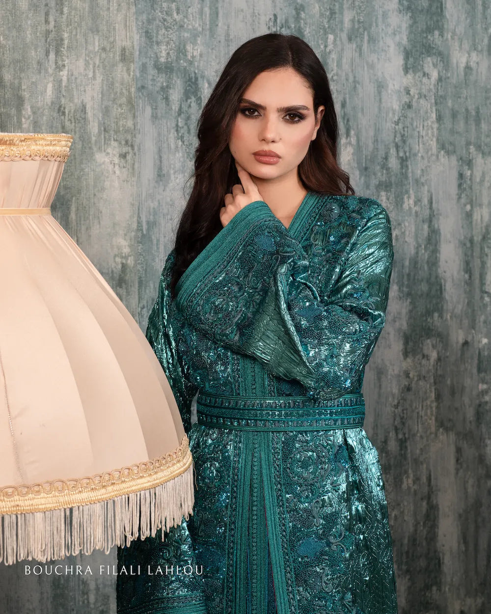 Model posing in a luxury green caftan with elaborate embroidery, showcasing the shimmering brocade fabric under soft lighting.