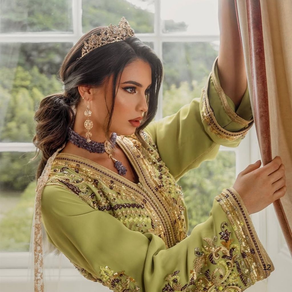 A green Moroccan caftan with embroidered neckline and cuffs, worn beside a window.