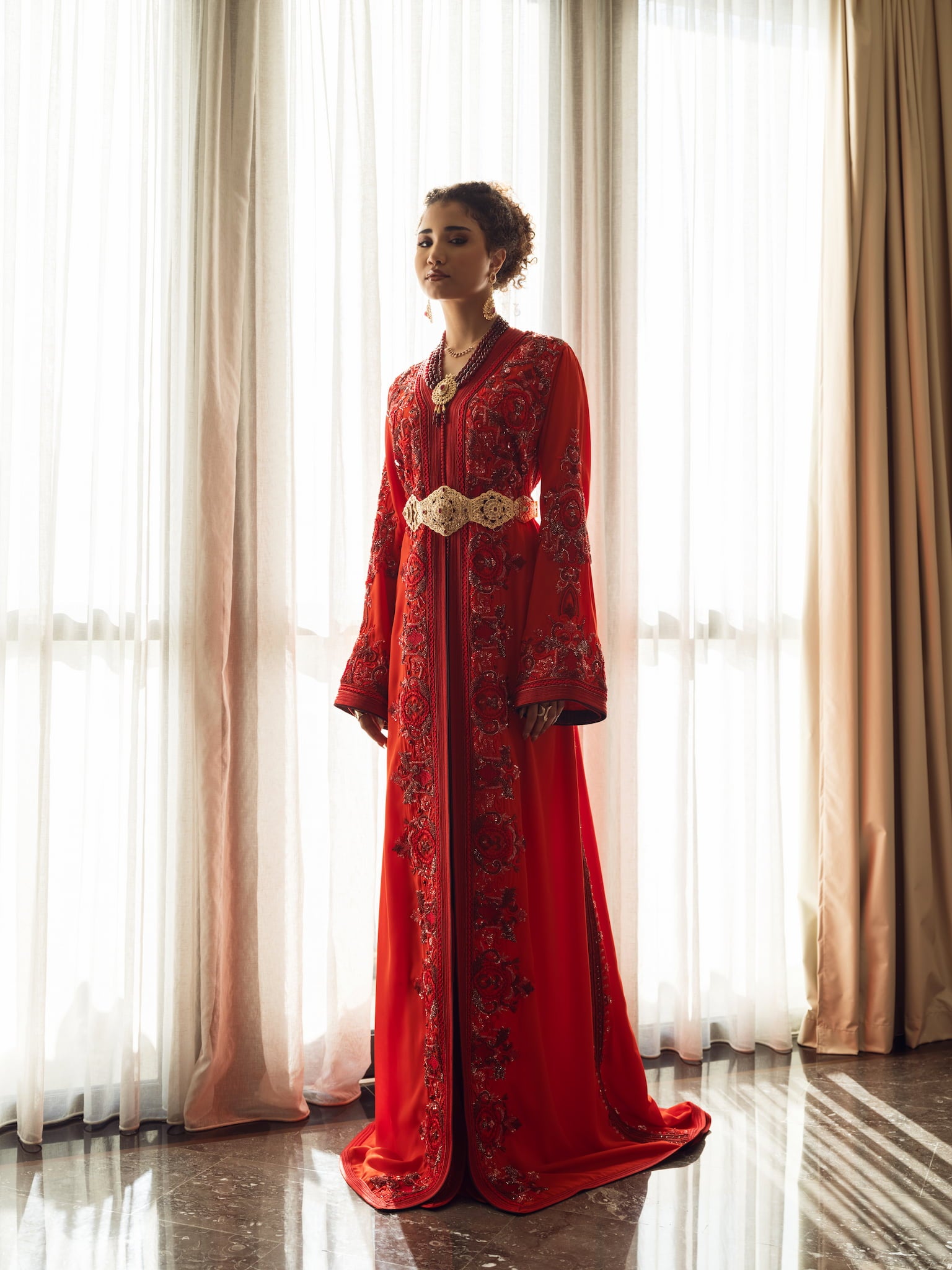 Deep ruby red Moroccan couture kaftan with elongated silhouette and gold embroidery, full-length view